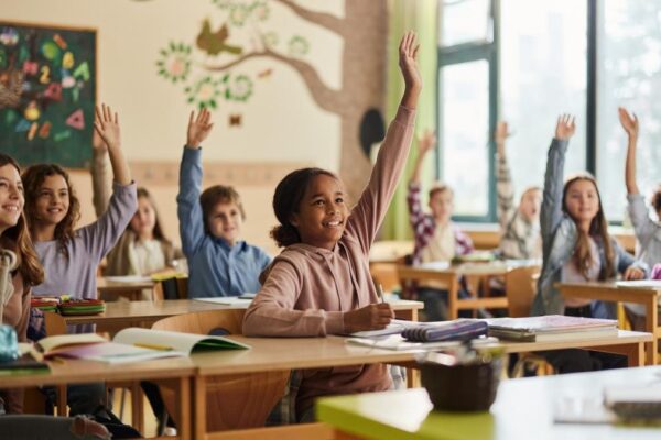 Kinderen in de klas. Een meisje steekt haar hand op.